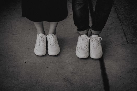 Black and white photo of two people standing in sneakers on pavement.