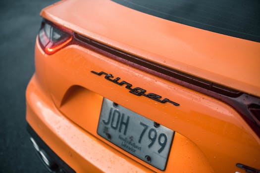 Detail shot of an orange car's rear showcasing raindrops and license plate.