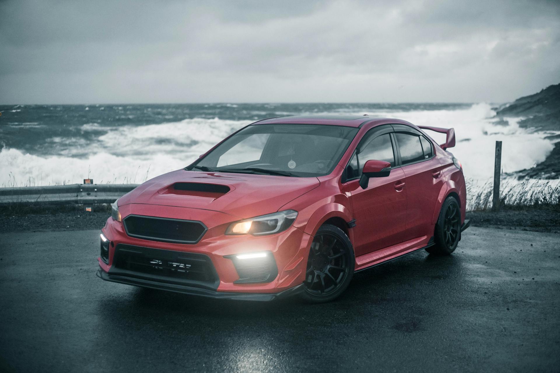 A red sports car parked by the ocean on a cloudy day, showcasing luxury and style.