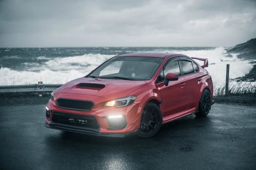 Free A red sports car parked by the ocean on a cloudy day, showcasing luxury and style. Stock Photo