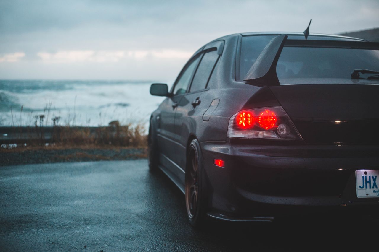 a dark car parked by a stormy ocean on a rainy day captures a serene y