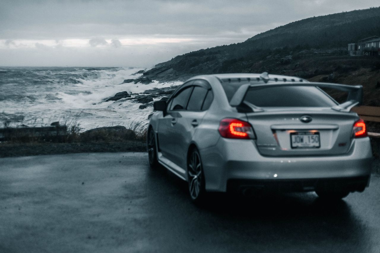 a sleek silver car parked near a crashing ocean on a moody overcast da