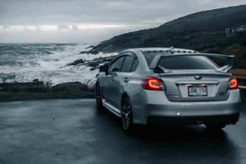 Free A sleek silver car parked near a crashing ocean on a moody, overcast day. Stock Photo