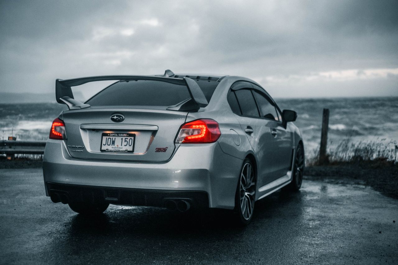 a gray subaru car parked near the ocean with a gloomy sky and wet asph