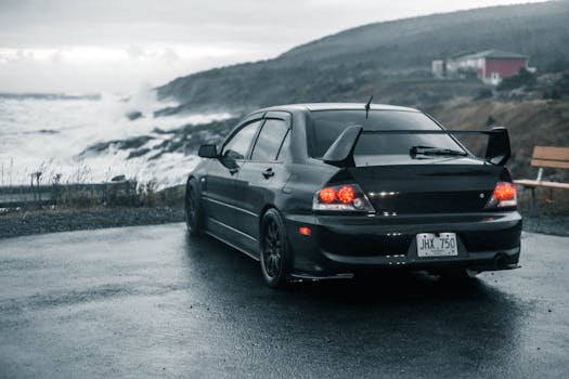 A sleek black car parked by the ocean amidst a moody, overcast setting, evoking a sense of adventure.