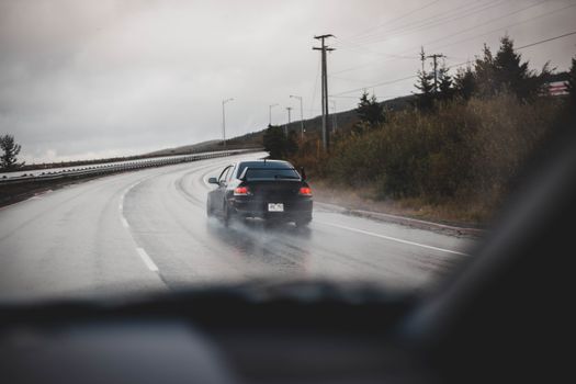 A black car drives on a rainy highway, showcasing speed and transportation.