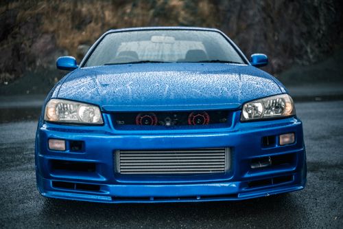 Free Front view of a blue sports car with headlights on a wet asphalt road after rain. Stock Photo