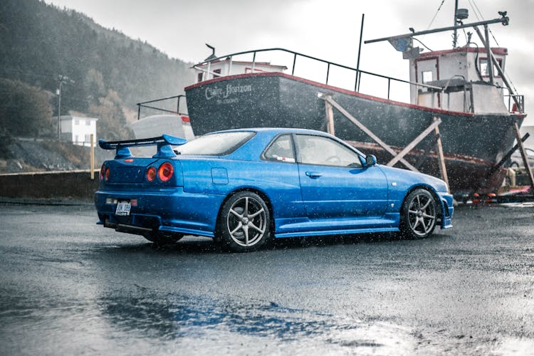 A Blue Car Parked Near A Boat 