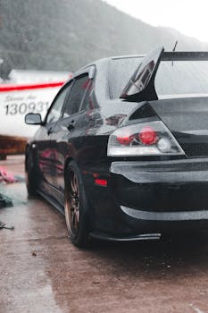 Close-up of a black sports car with raindrops, showcasing its sleek design.