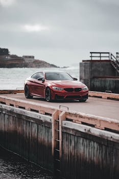 Red sports car on a dock under a dramatic, moody sky, showcasing its sleek design and waterfront location.