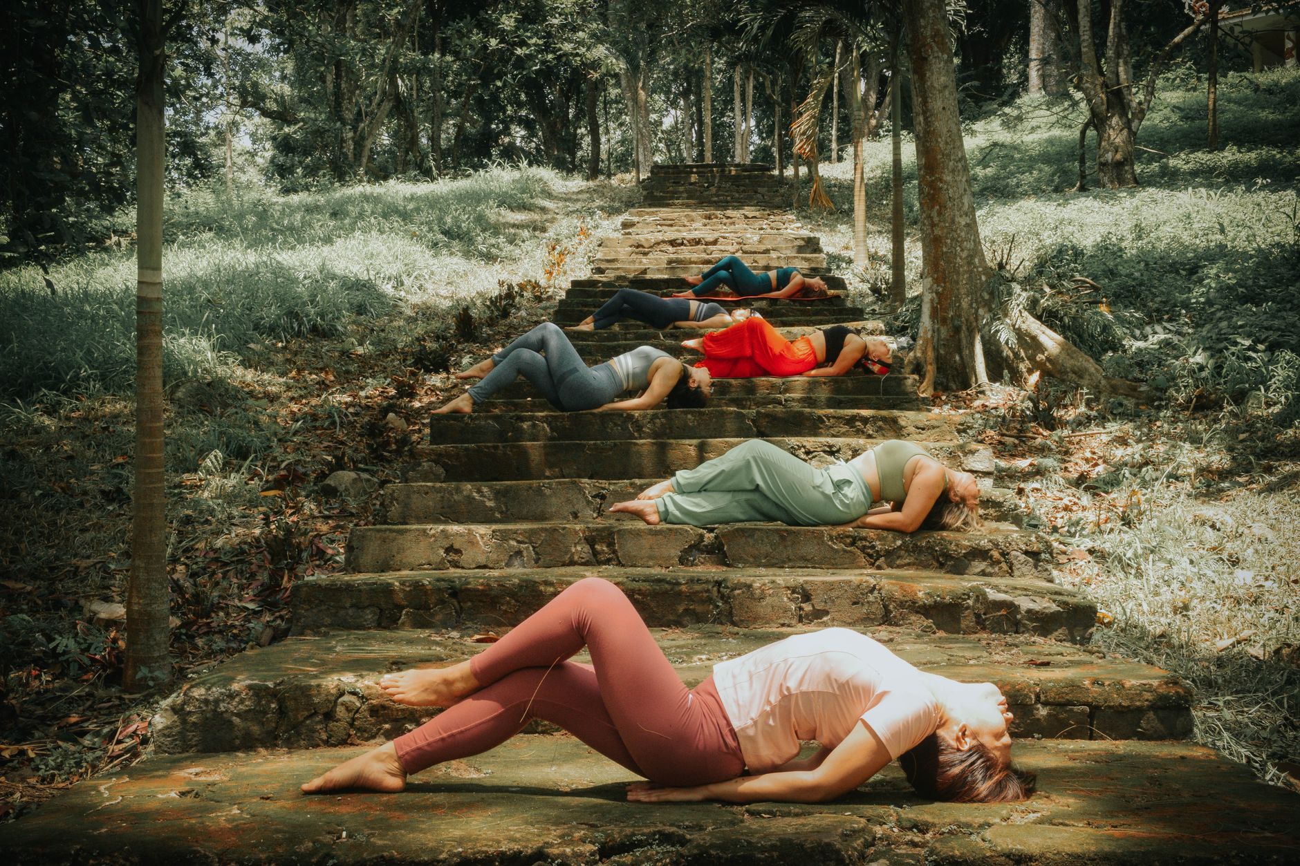 Group of women in yoga poses lying on stone stairs in a serene forest atmosphere.
