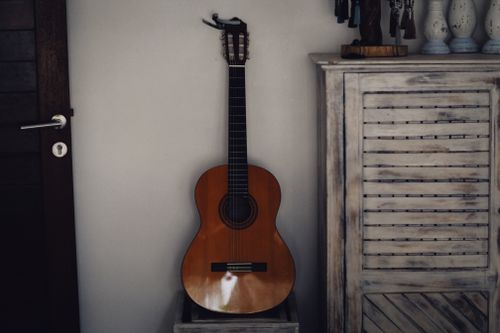 Free Acoustic guitar resting in a cozy home interior beside a rustic dresser. Stock Photo