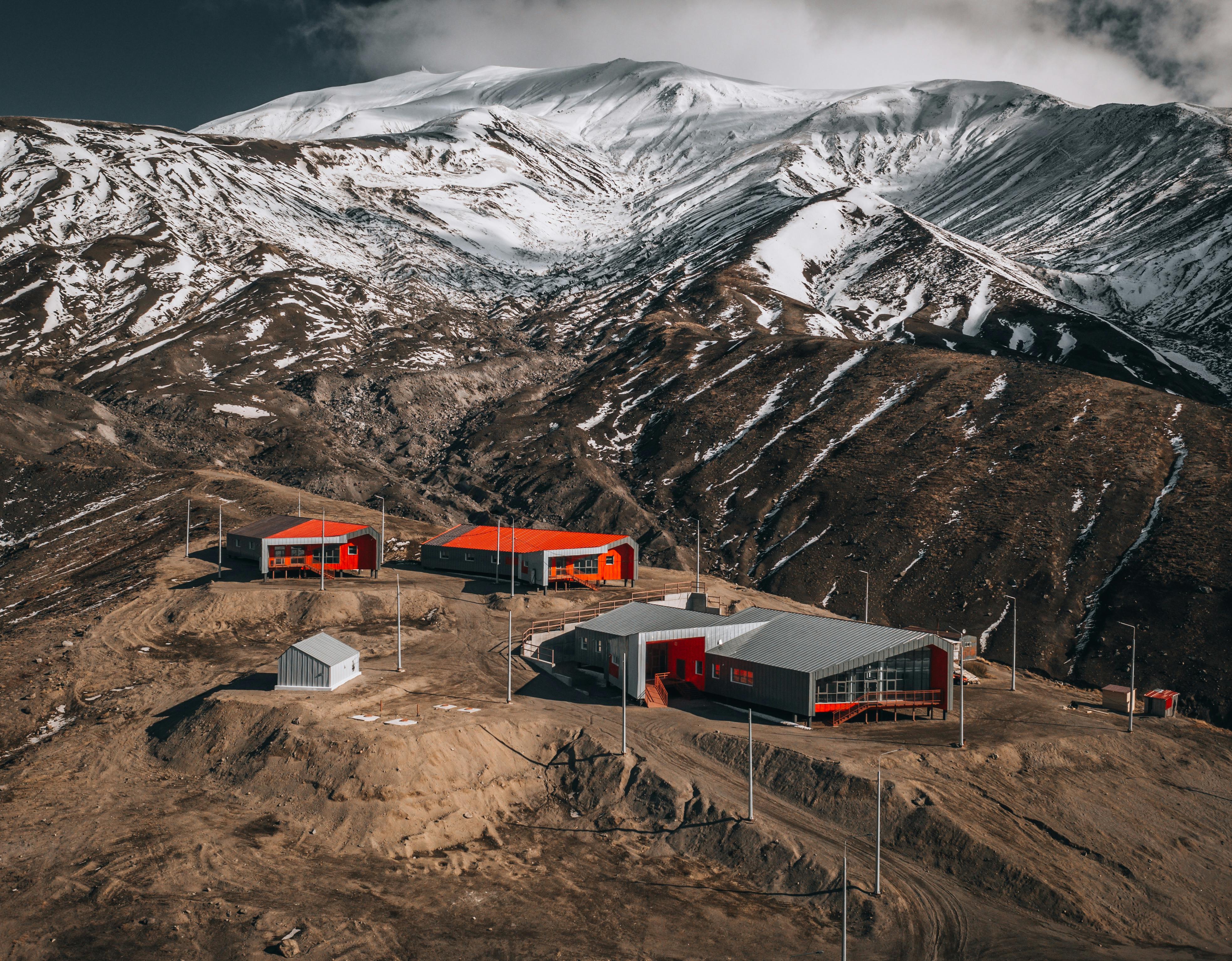 Aerial view of a remote settlement with red buildings near snow-capped mountains.