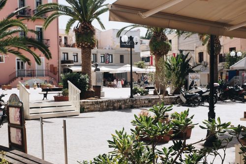 Free Vibrant square in Chania, Greece, showcasing palm trees, cafes, and charming architecture. Stock Photo