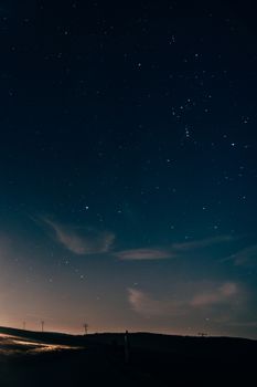 A serene starry night sky over rolling hills, with a silhouette beneath the vibrant blanket of stars.