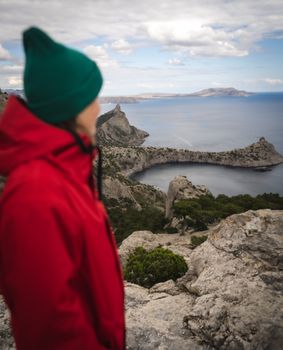 Woman in red jacket gazing at a breathtaking coastal view from a rocky cliff.