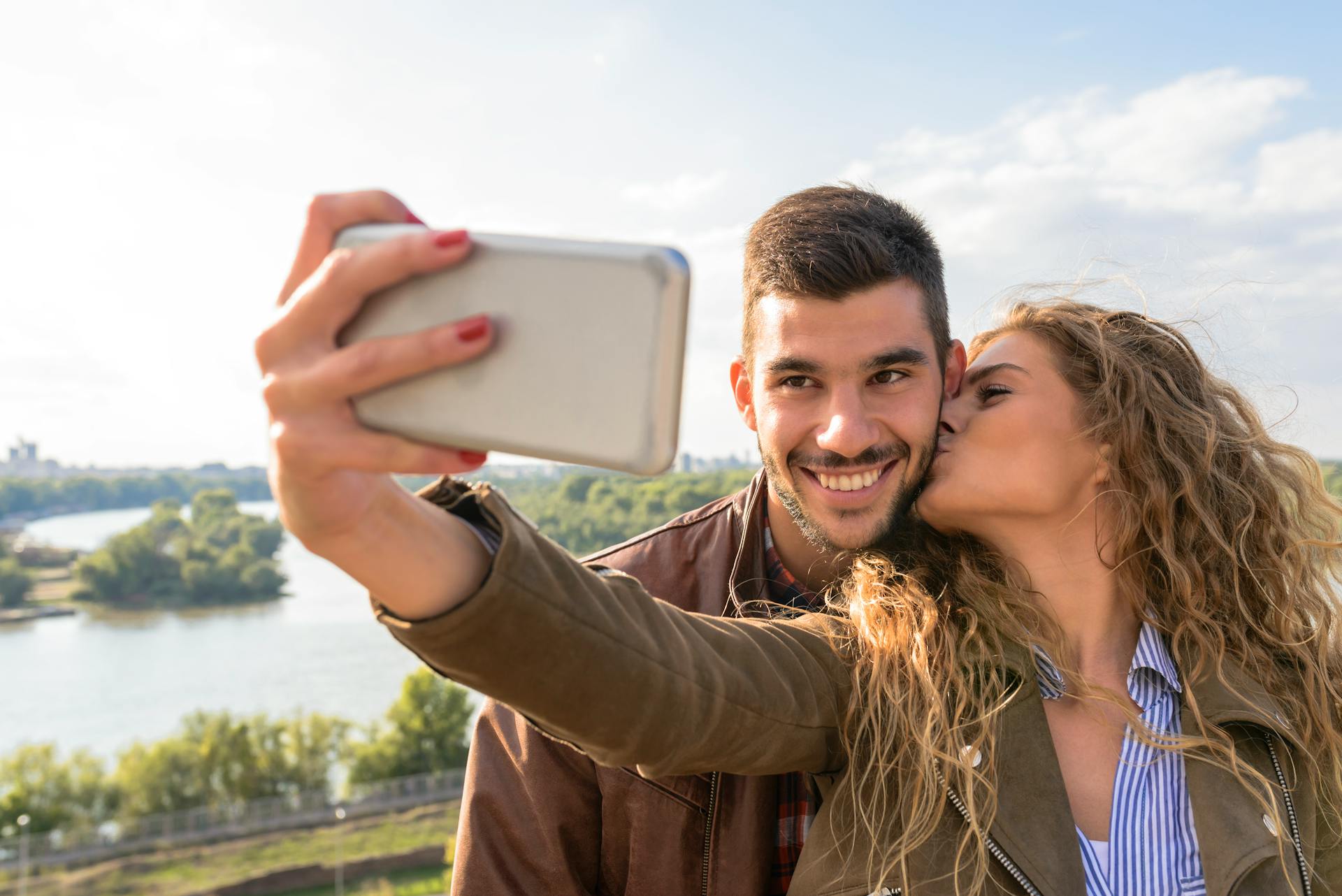 Ett lyckligt par tar en romantisk selfie vid den natursköna flodstranden en solig dag.