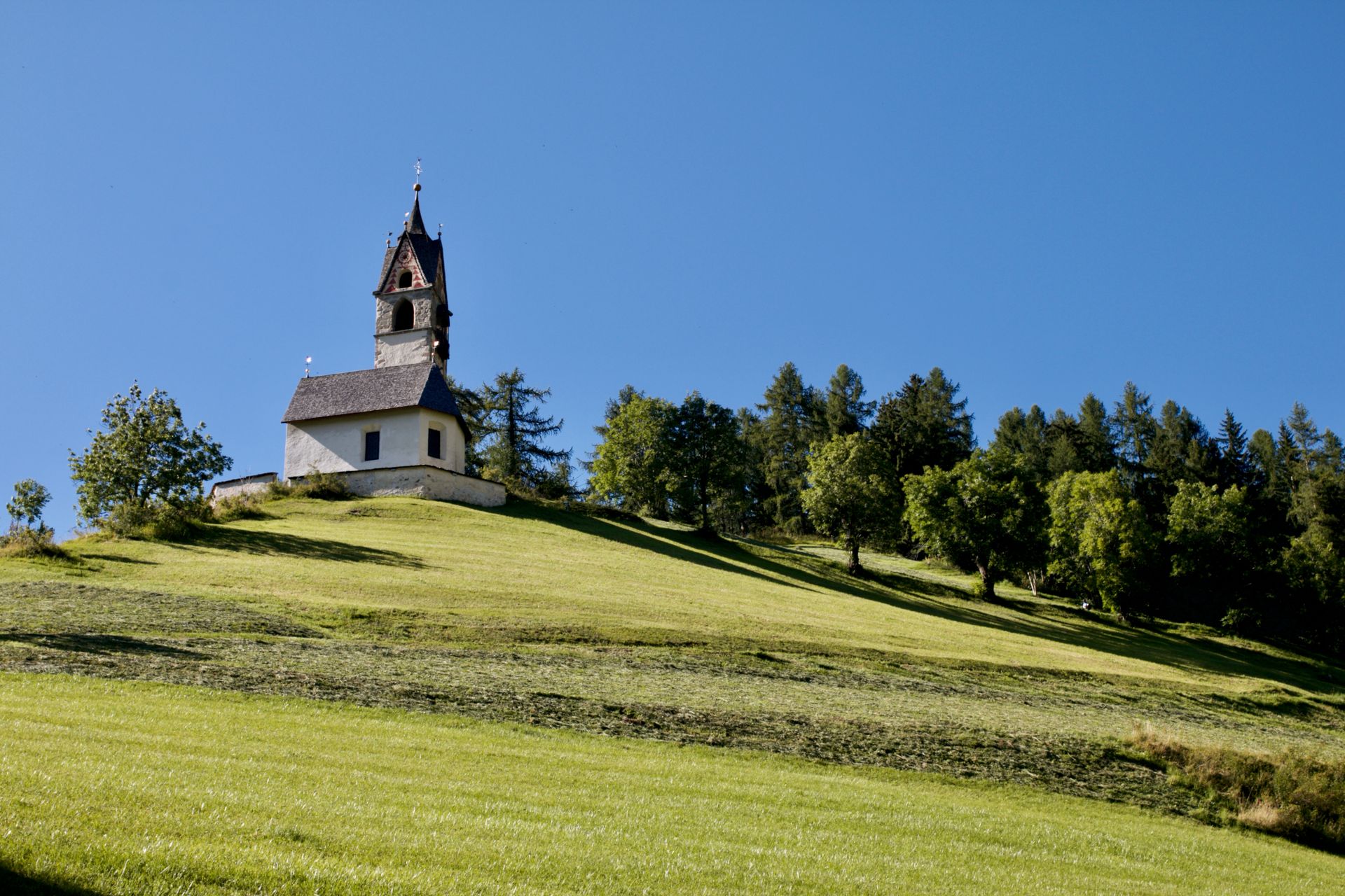 Idyllic landscape with St Barbara Church on a hilltop in Trentino-Alto Adige under clear blue skies.
