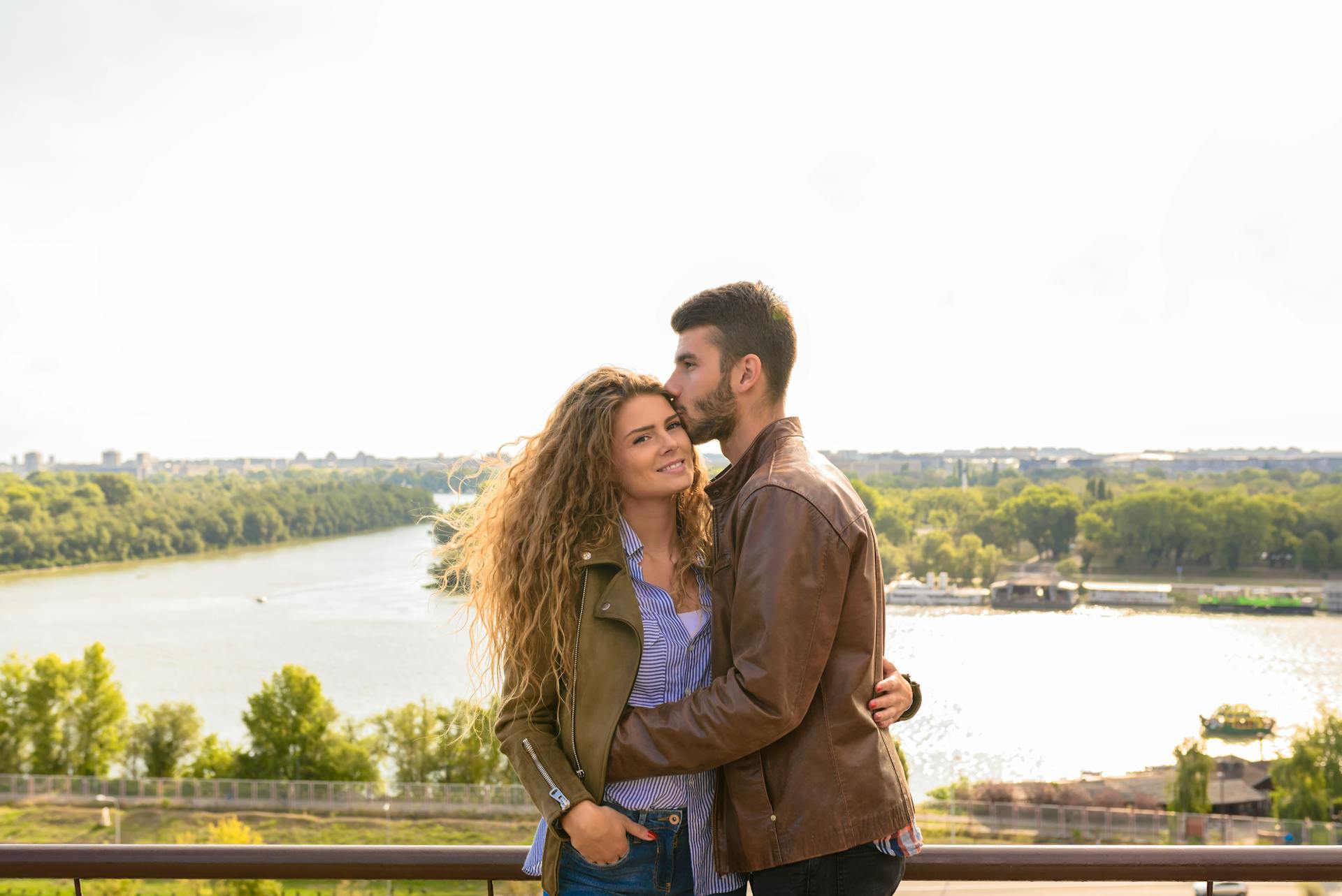 Couple embracing on a riverside overlook with bright, romantic ambiance.