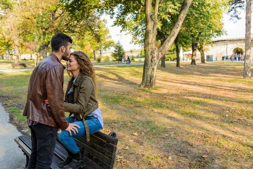Free A loving couple enjoys a tender moment on a park bench surrounded by autumn trees. Stock Photo