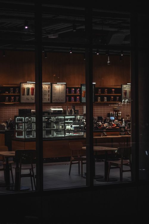 Free Quiet café interior at night with glass panels and warm lighting, perfect for cozy atmosphere concepts. Stock Photo