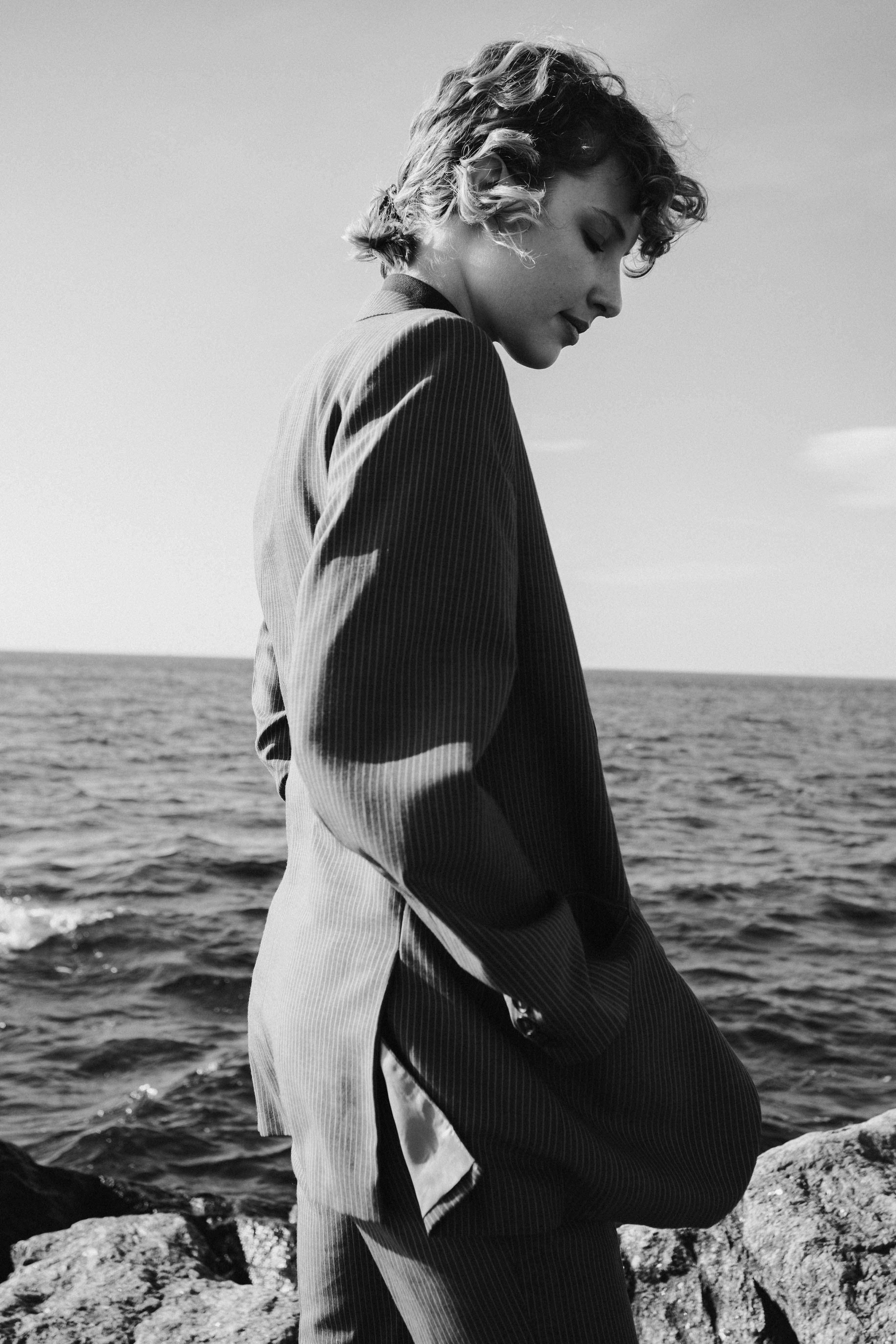 Elegant grayscale portrait of a person by the ocean shore, exuding contemplative mood.