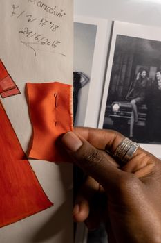 Close-up of a designer's hand holding an orange fabric swatch against a mood board.