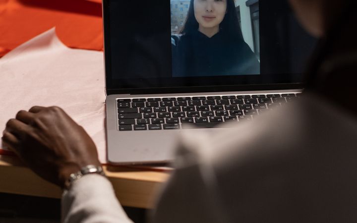 A woman in a creative workspace on a video call with a colleague on a laptop.