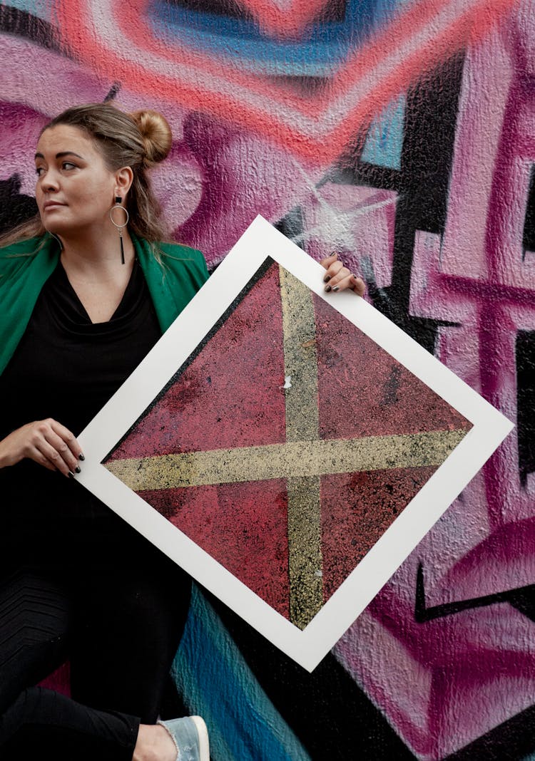 A Woman Holding A Poster While Leaning On A Graffiti Wall