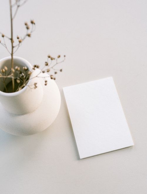 Free Minimalist scene with a white vase and blank paper, perfect for design mockups. Stock Photo