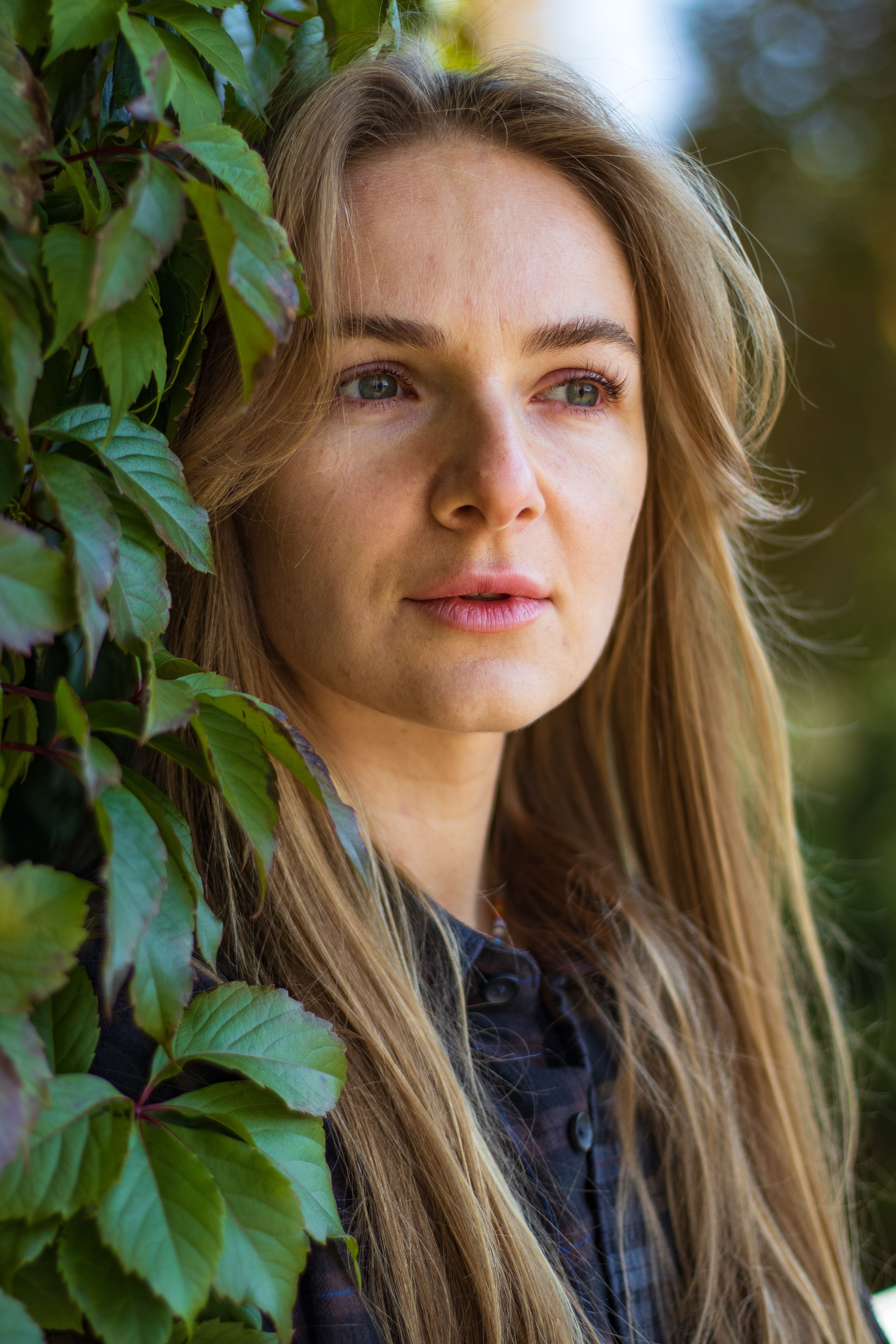 Close-up portrait of a woman surrounded by green leaves in an outdoor setting.