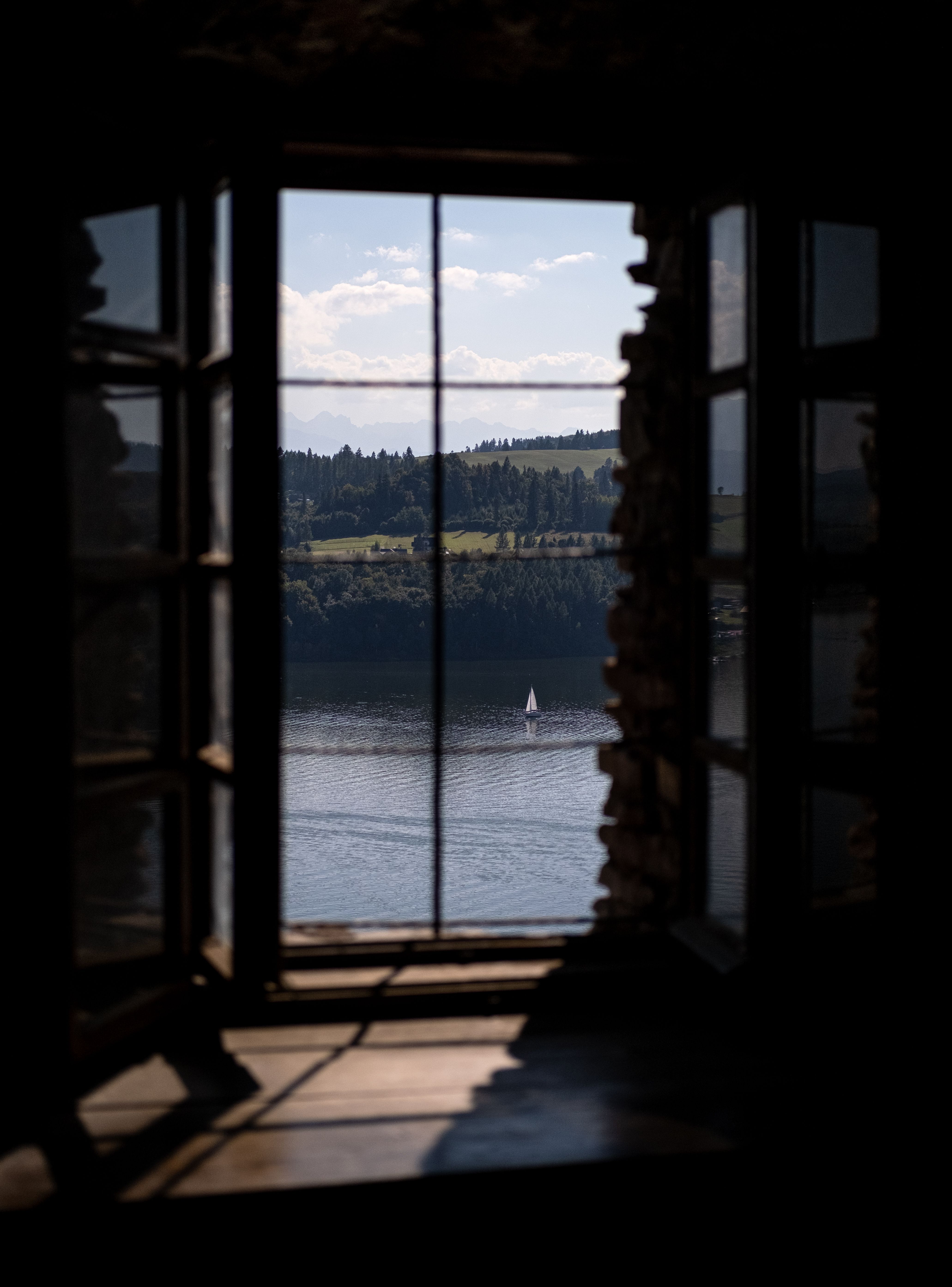 Charming countryside view of a lake with a distant sailboat seen through a rustic window.
