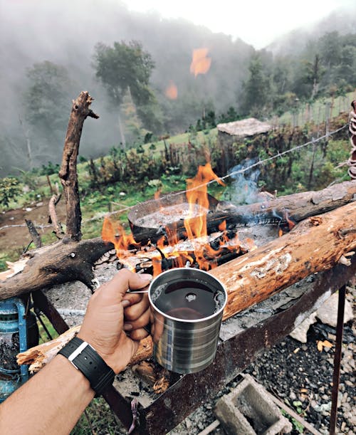 Free Person Holding Stainless Tin Cup Near the Campfire Stock Photo