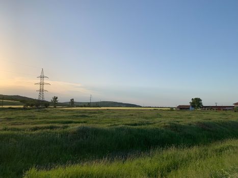 A peaceful rural scene featuring a lush green field at sunset with distant hills and power lines.