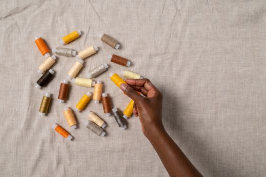 A diverse hand holding threads in various colors on a beige fabric surface, showcasing creativity and craftsmanship.