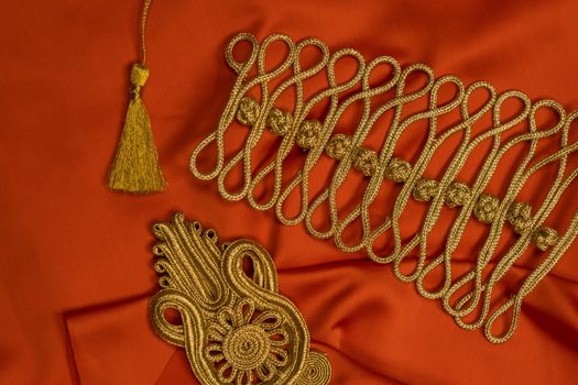 Flat lay of intricate golden embroidery designs on vibrant orange fabric, showcasing craftsmanship.