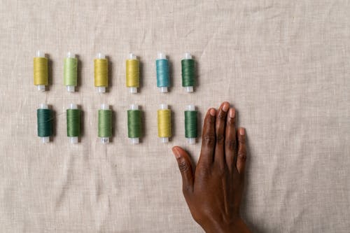 A Flat lay of Sewing Threads Next to a Female Black Hand 