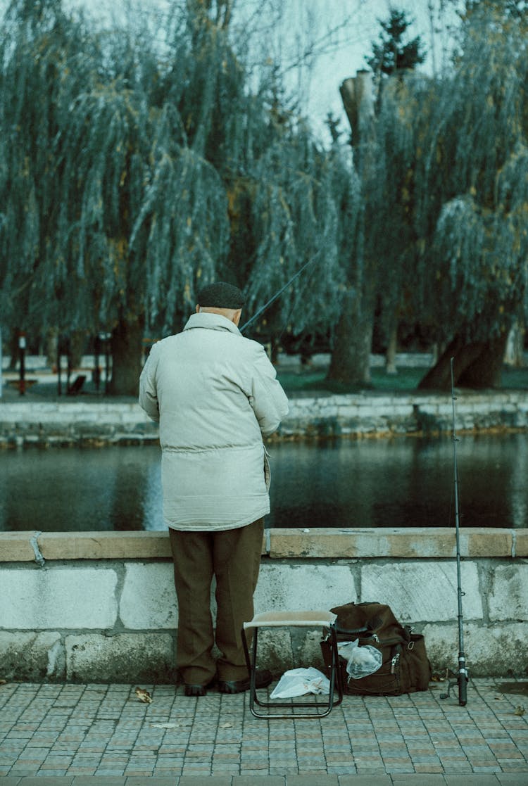 Senior Man Standing And Fishing In Park Pond