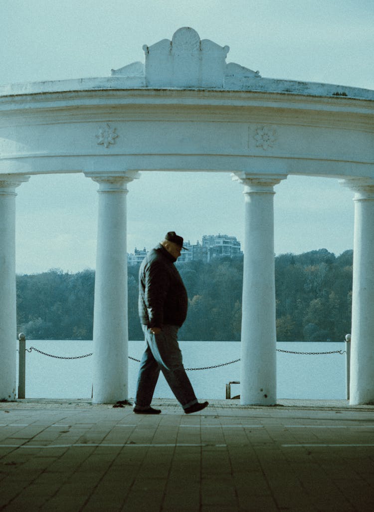 Senior Man Walking Along Colonnade At Sea Embankment