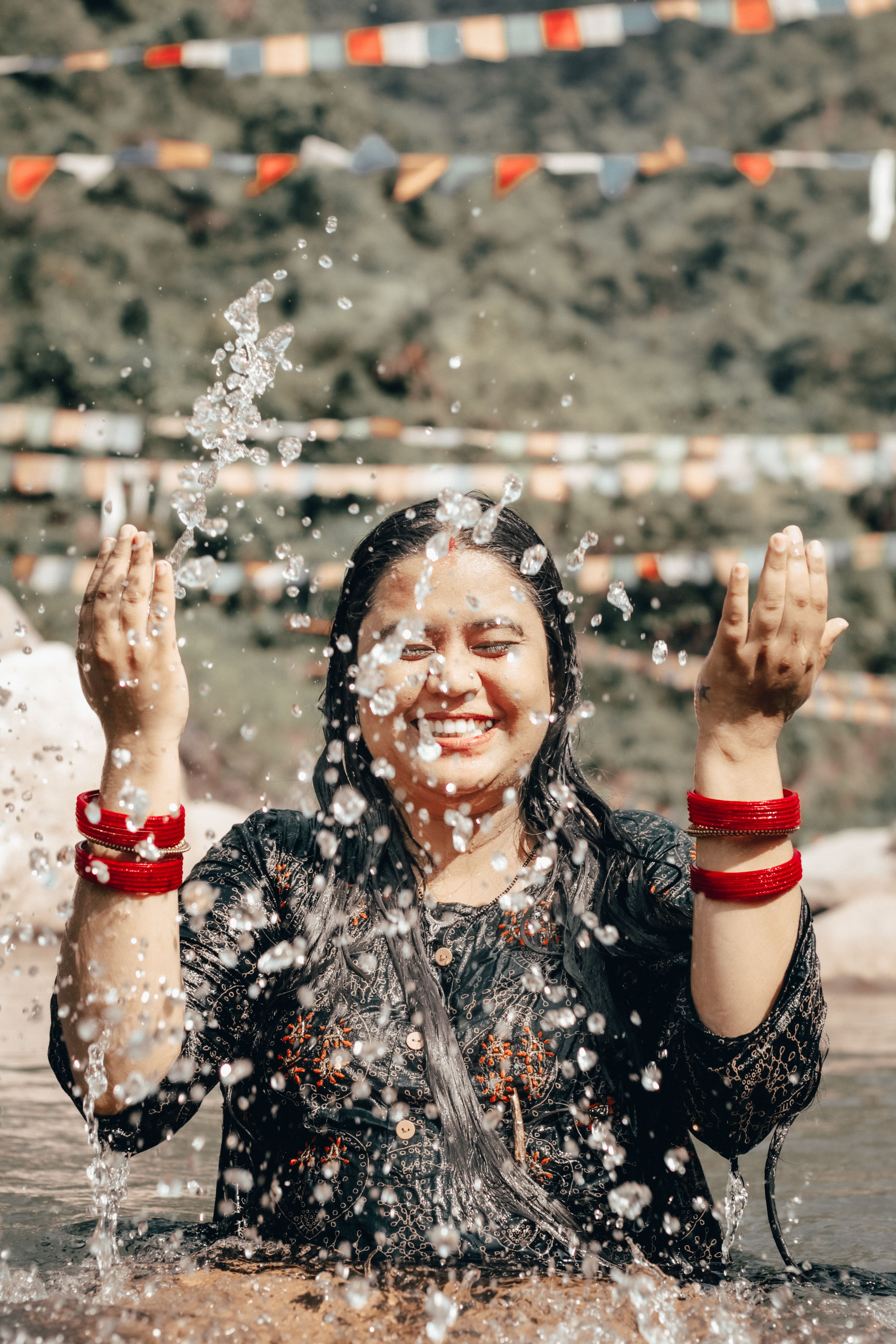 Asian woman joyfully splashing water outdoors, smiling amidst colorful flags.