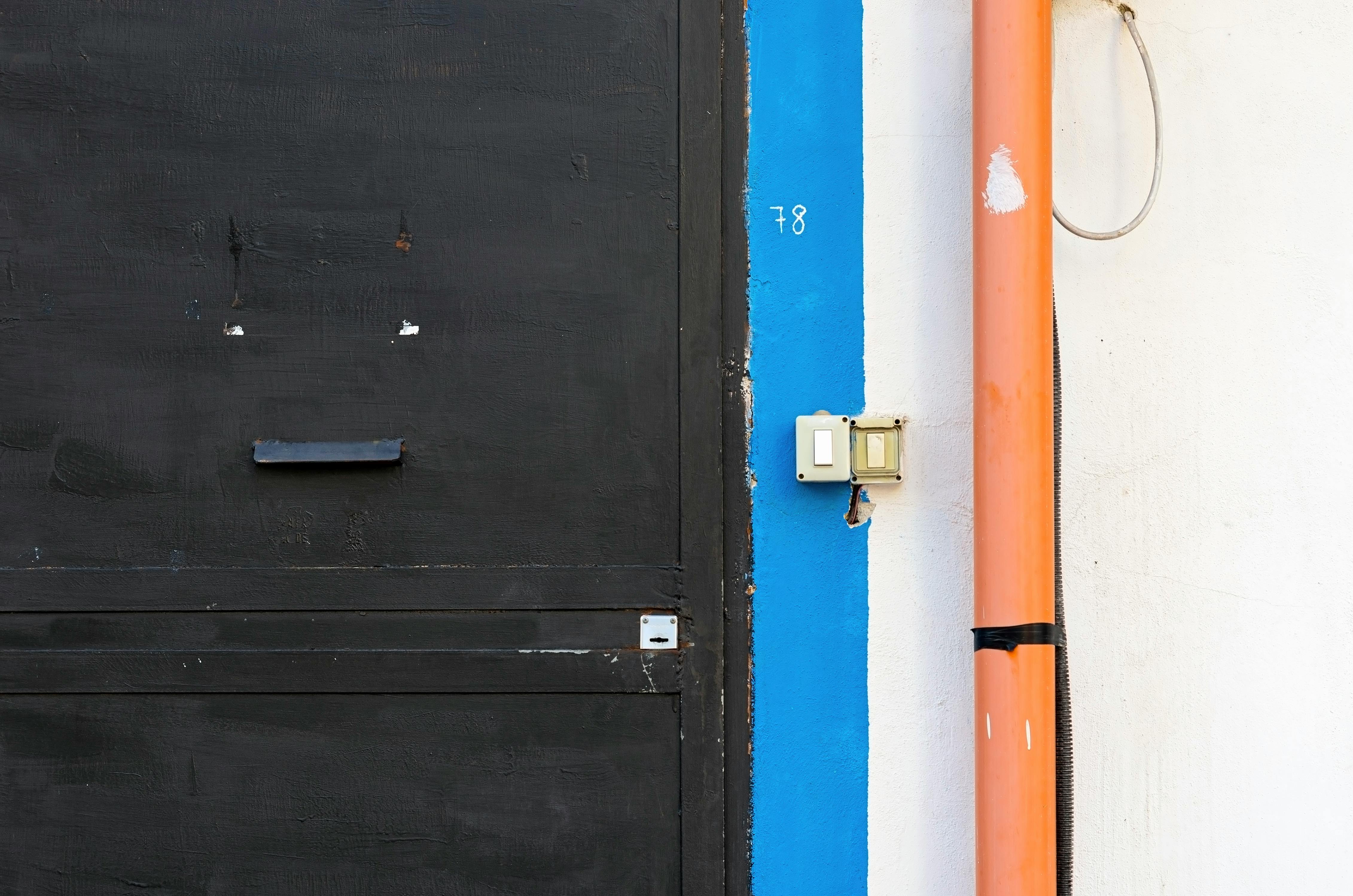 Industrial style black door with a vibrant orange pipe and blue accent wall.
