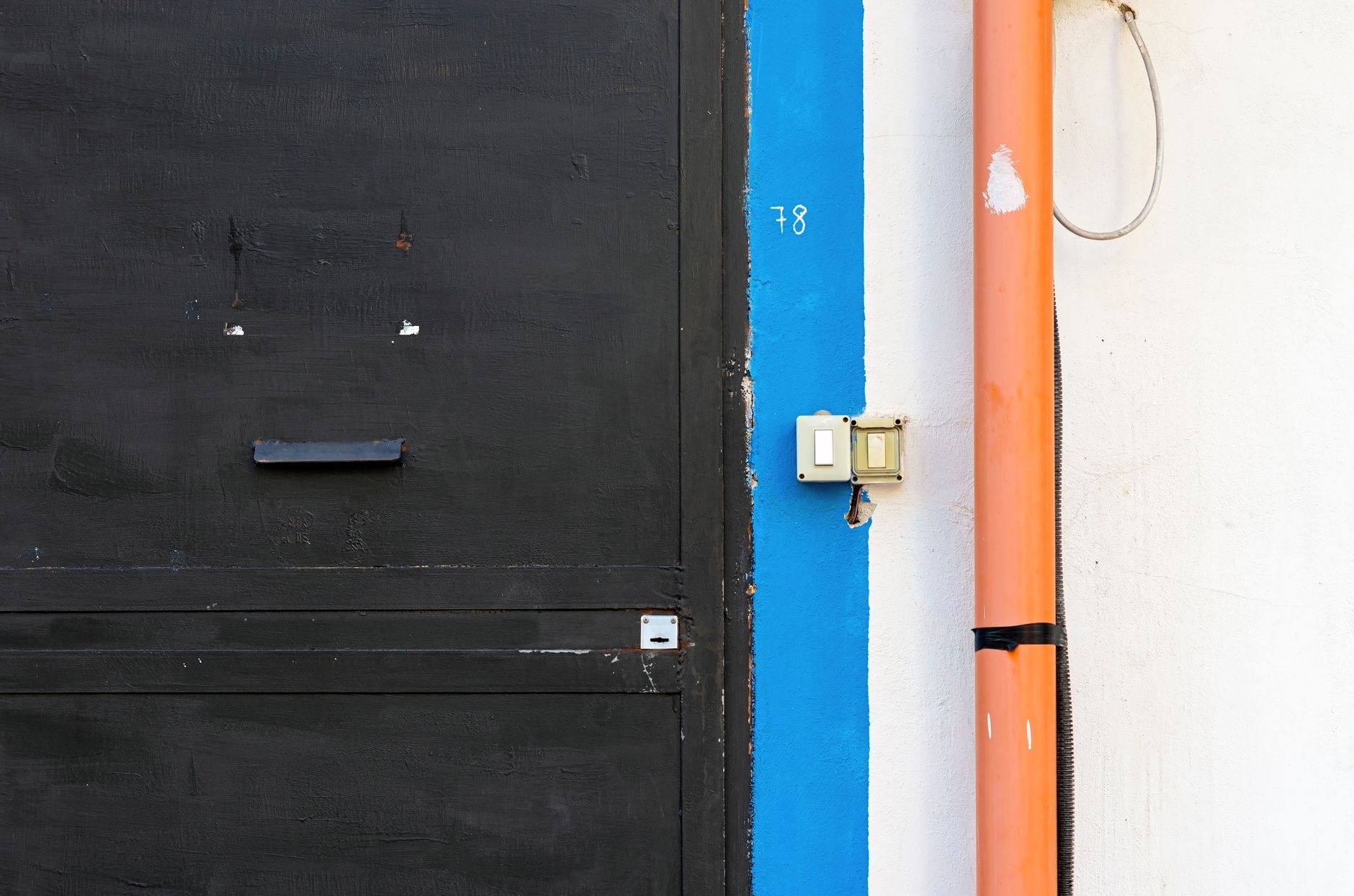 Industrial style black door with a vibrant orange pipe and blue accent wall.
