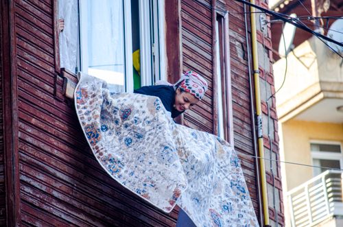 Free An adult woman cleaning a carpet outside a window in a vibrant city setting. Stock Photo