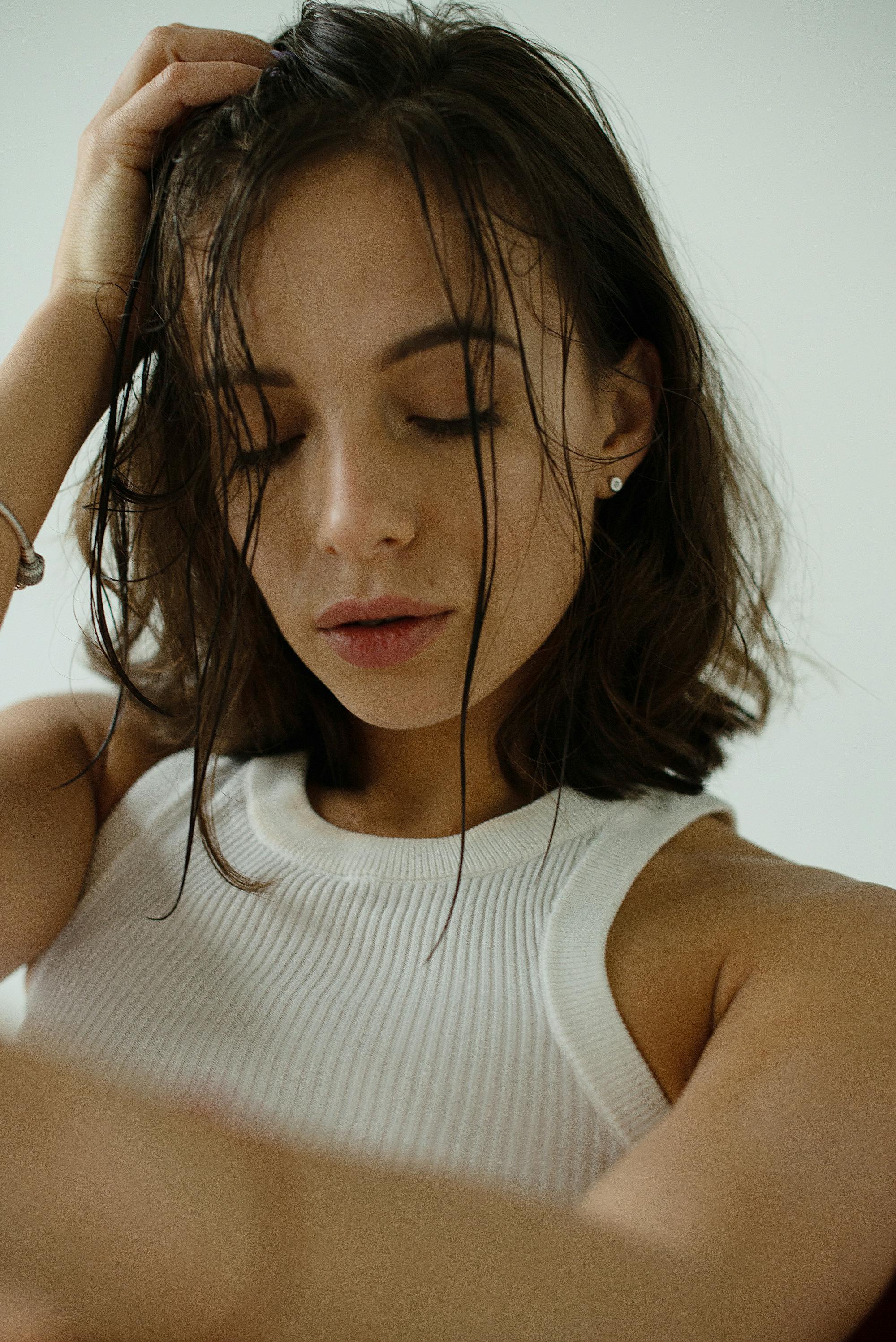 A serene portrait of a young woman with closed eyes, wearing a white top, exuding elegance and tranquility.