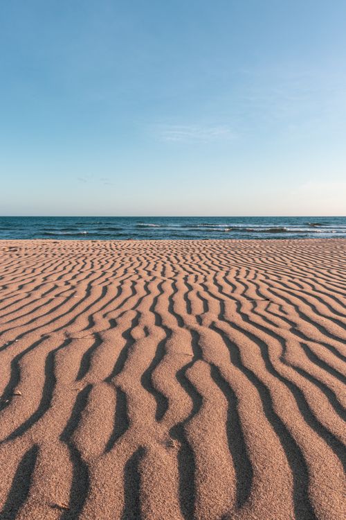 Free Beautiful sandy beach with wavy patterns and calm sea under a clear sky at sunrise, perfect for relaxation and tranquility. Stock Photo