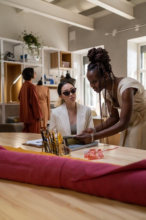Free Women engaged in a fashion design meeting inside a contemporary studio with tailoring tools. Stock Photo