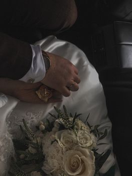 Close-up of a couple holding hands with a rose bouquet, capturing an intimate wedding moment.