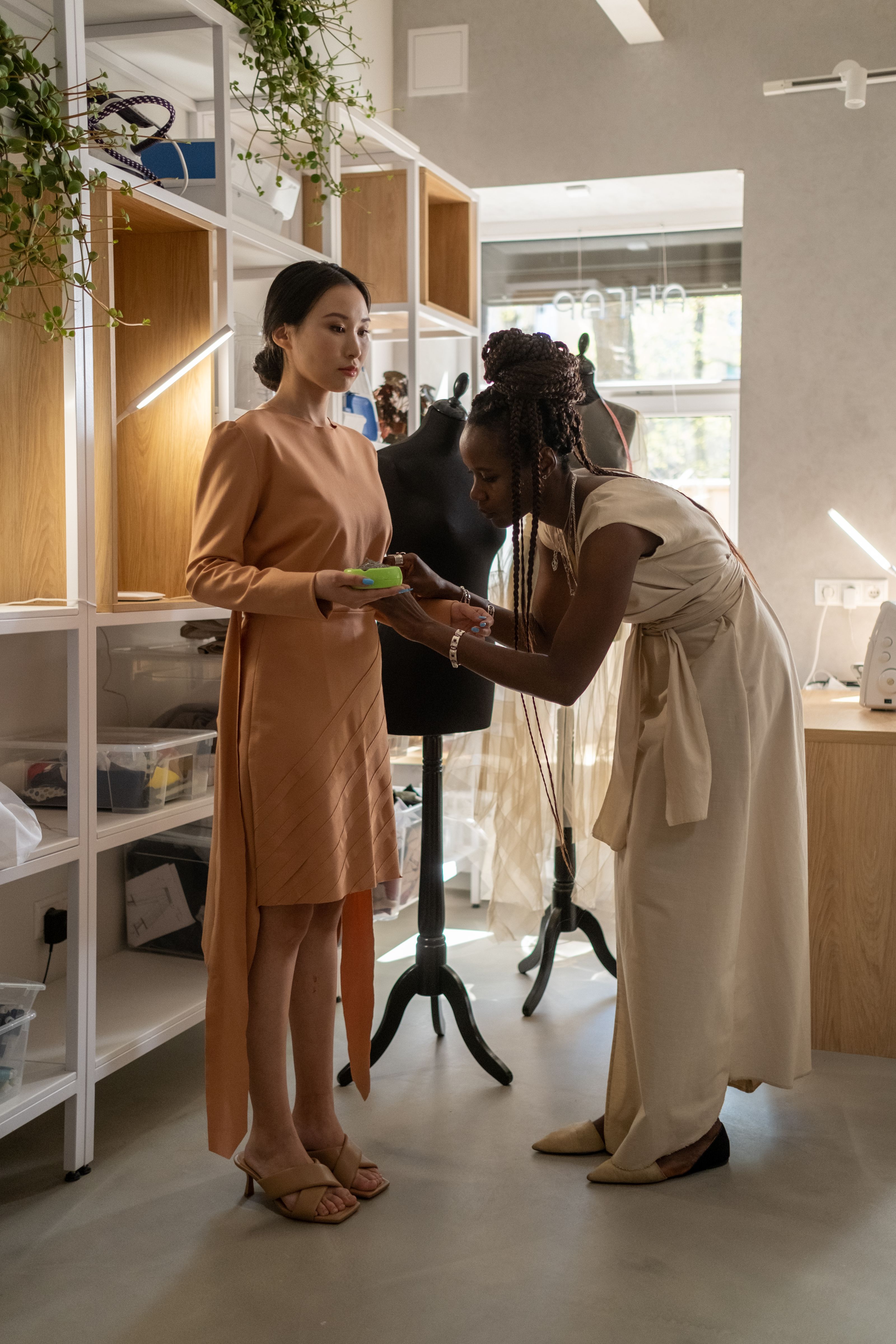 Um designer de moda ajustando um vestido em uma cliente em um ateliê moderno.