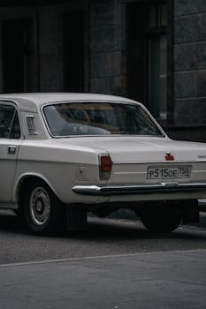 A close-up of a classic white vintage car parked on an urban street with a moody atmosphere.