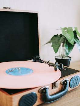 Close-up of a vintage turntable playing a pink vinyl record beside a houseplant.